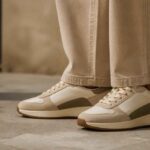 Beżowe sneakersy na nogach osoby ubranej w jasne spodnie, stojącej na betonowej podłodze